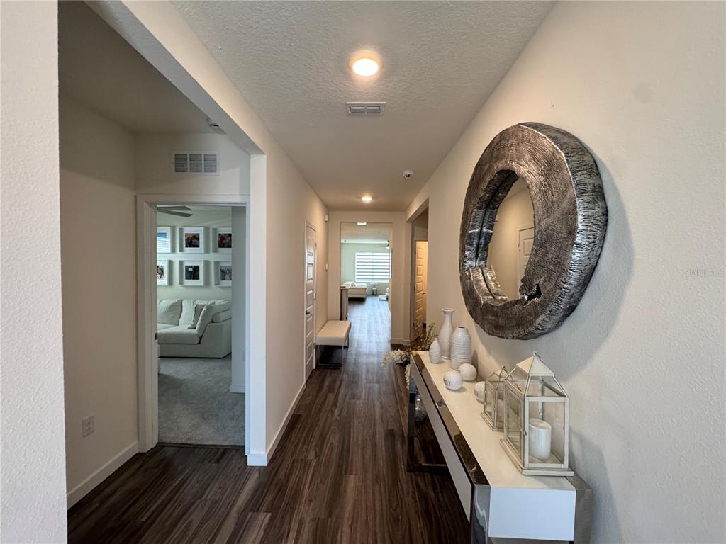 A hallway with wood-look flooring leads to a living area, featuring a large circular mirror — 415 TALISI LOOP, ST CLOUD, FL