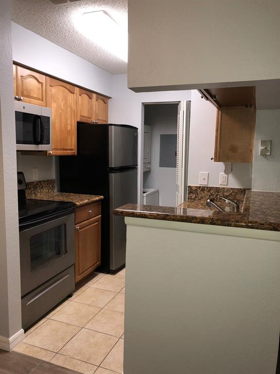 A kitchen features wood cabinets, stainless steel appliances, granite countertops, and tile flooring — 224 AFTON SQUARE UNIT 304, ALTAMONTE SPRINGS, FL