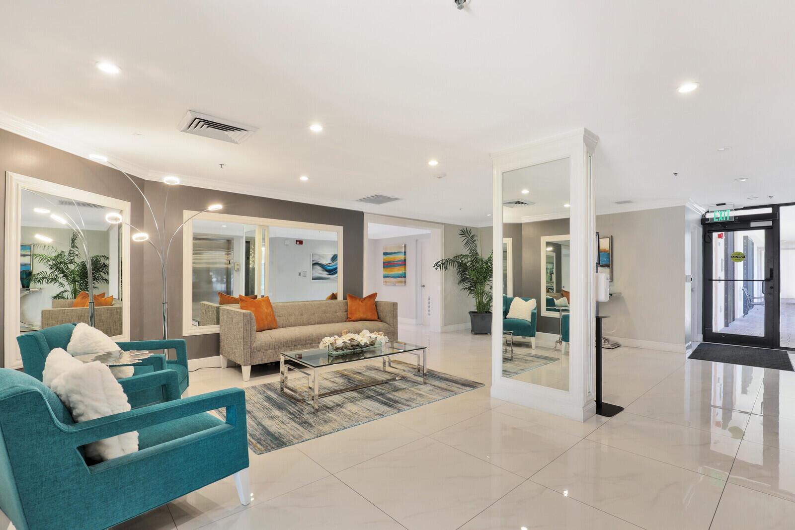 A modern lobby features teal armchairs, a gray sofa, a glass coffee table, and mirrors — 2687 N Ocean Boulevard # 305, Boca Raton FL 33431, BOCA RATON, FL