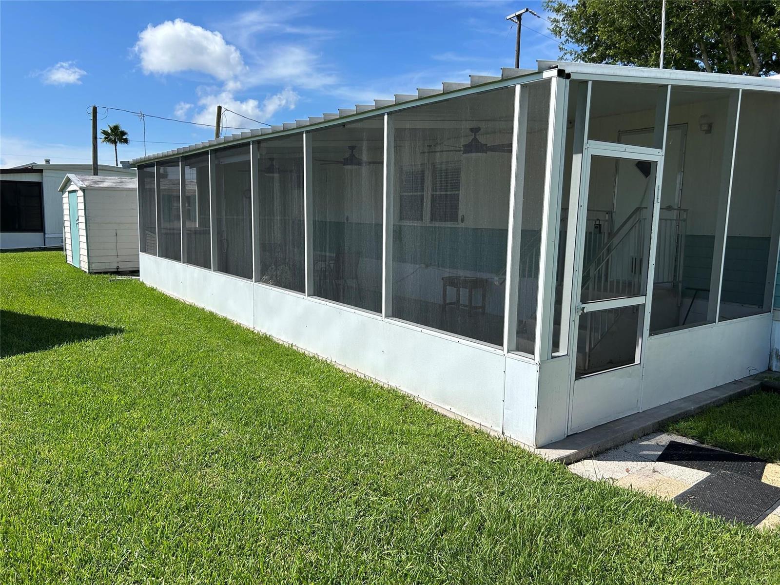 A white screened-in porch is attached to a mobile home next to a small shed — 1379 Chobee Street, Okeechobee FL 34974, OKEECHOBEE, FL