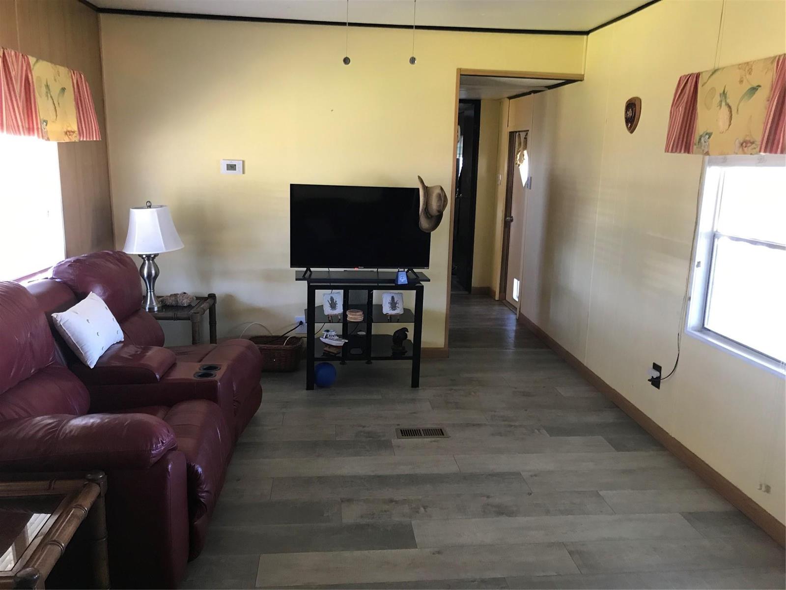 A living room features yellow walls, wood-look flooring, a red leather sofa, and a television — 1379 Chobee Street, Okeechobee FL 34974, OKEECHOBEE, FL
