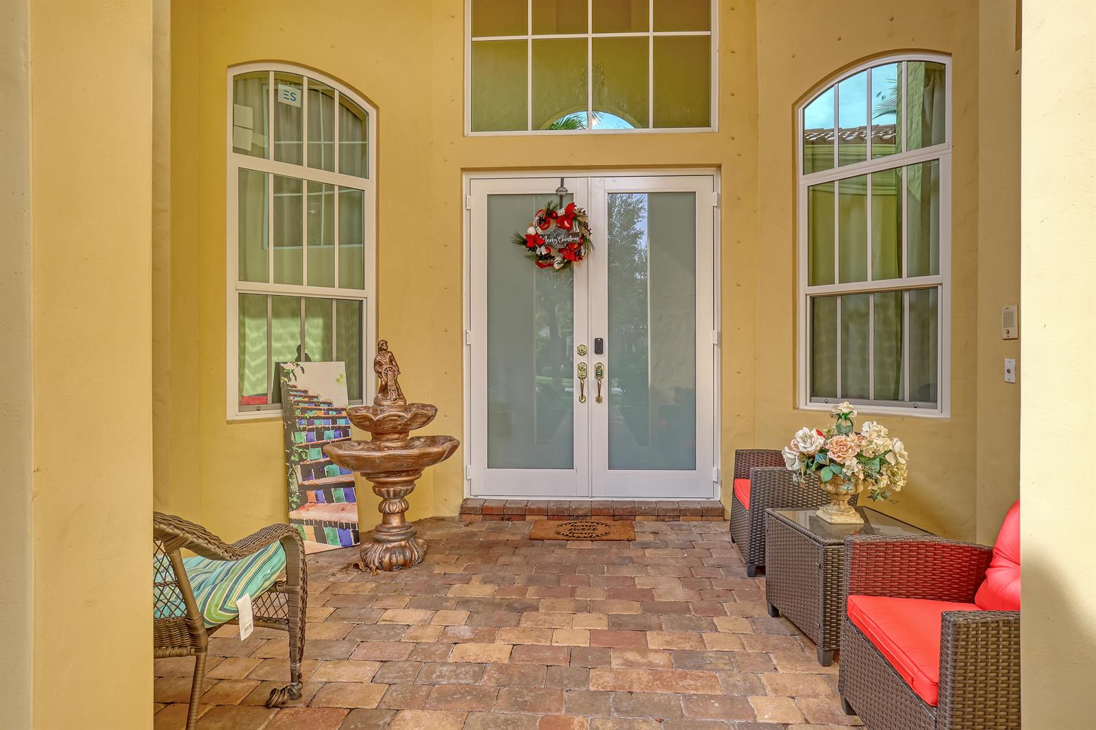 A paved entryway features a double glass door, a fountain, and outdoor wicker furniture — 3389 Lago De Talavera, Lake Worth FL 33467, LAKE WORTH, FL