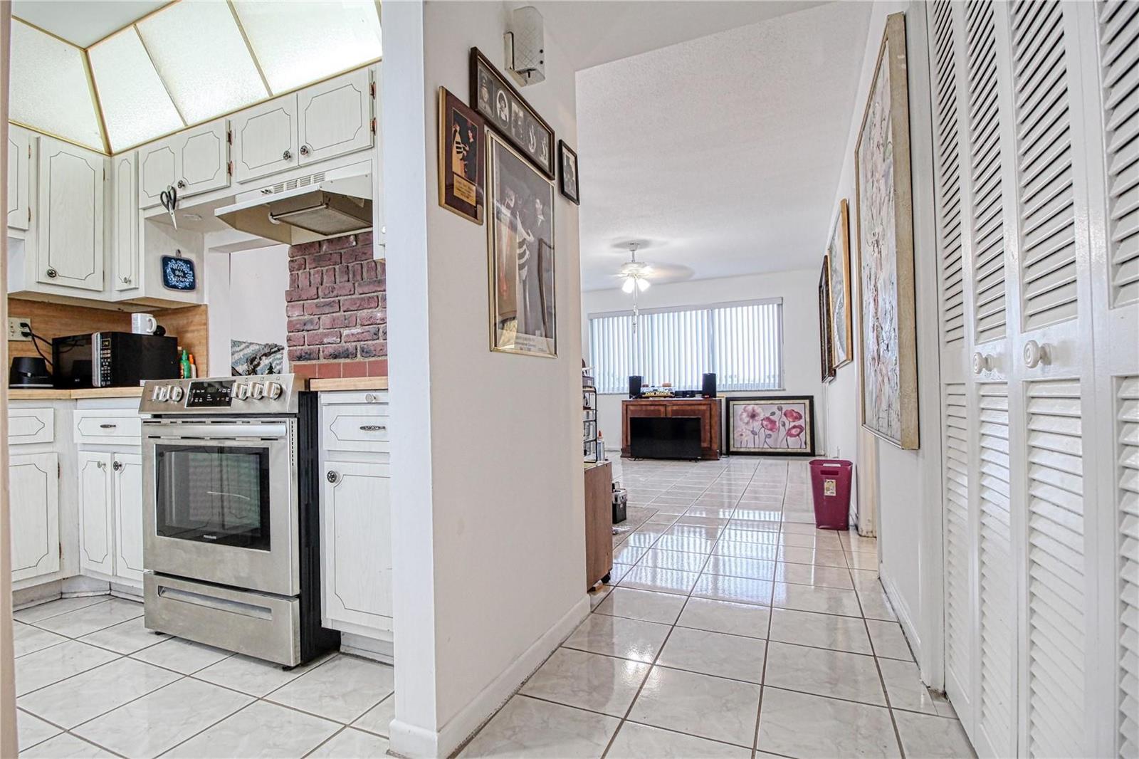 A kitchen with white cabinets and stainless steel appliances opens into a tiled living area — 2300 Park Lane # 311, Hollywood FL 33021, HOLLYWOOD, FL