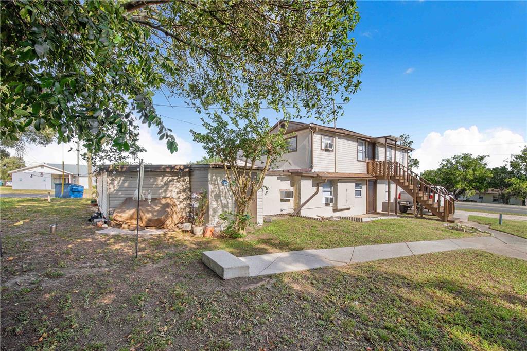 A two-story building with beige siding and an exterior wooden staircase stands on a lawn — 402 E MAIN STREET, DUNDEE, FL
