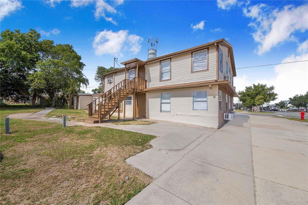 A two-story building with beige siding, an exterior wooden staircase, and a concrete parking area — 402 E MAIN STREET, DUNDEE, FL