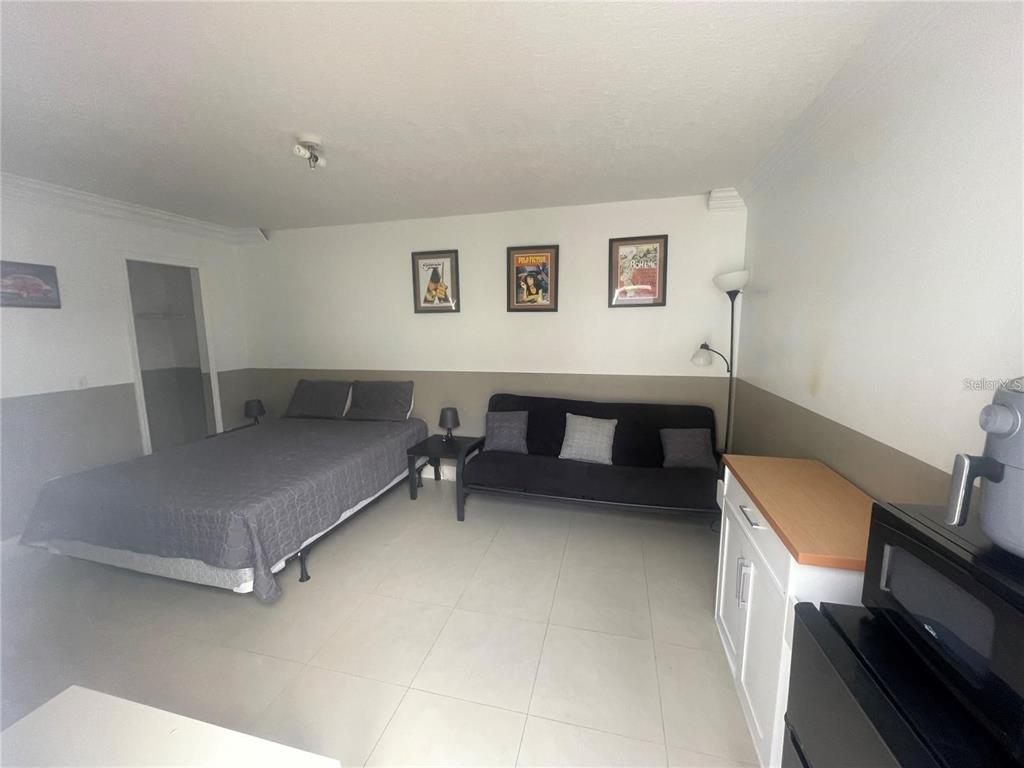 A studio room features a bed, a black futon, tiled floors, and a small kitchenette — 352 CARIBBEAN DRIVE UNIT Front, DAVENPORT, FL