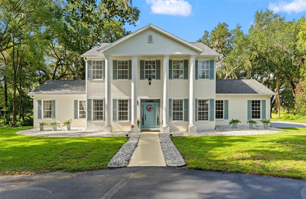 A two-story white house with four columns, blue shutters, and a central front door — 14050 GRANDEUR WAY, DADE CITY, FL