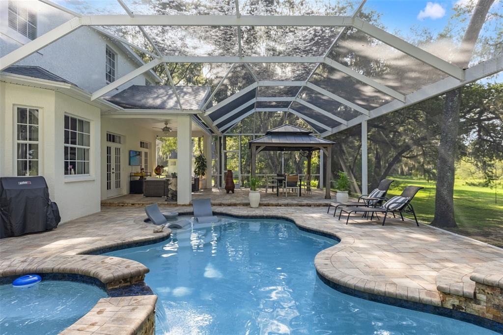 A screened-in patio features a swimming pool, hot tub, and a covered outdoor dining area — 14050 GRANDEUR WAY, DADE CITY, FL