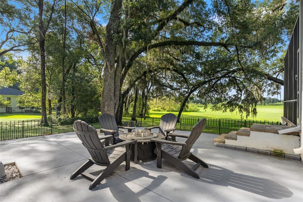 A concrete patio features four Adirondack chairs arranged around a central fire pit under trees — 14050 GRANDEUR WAY, DADE CITY, FL