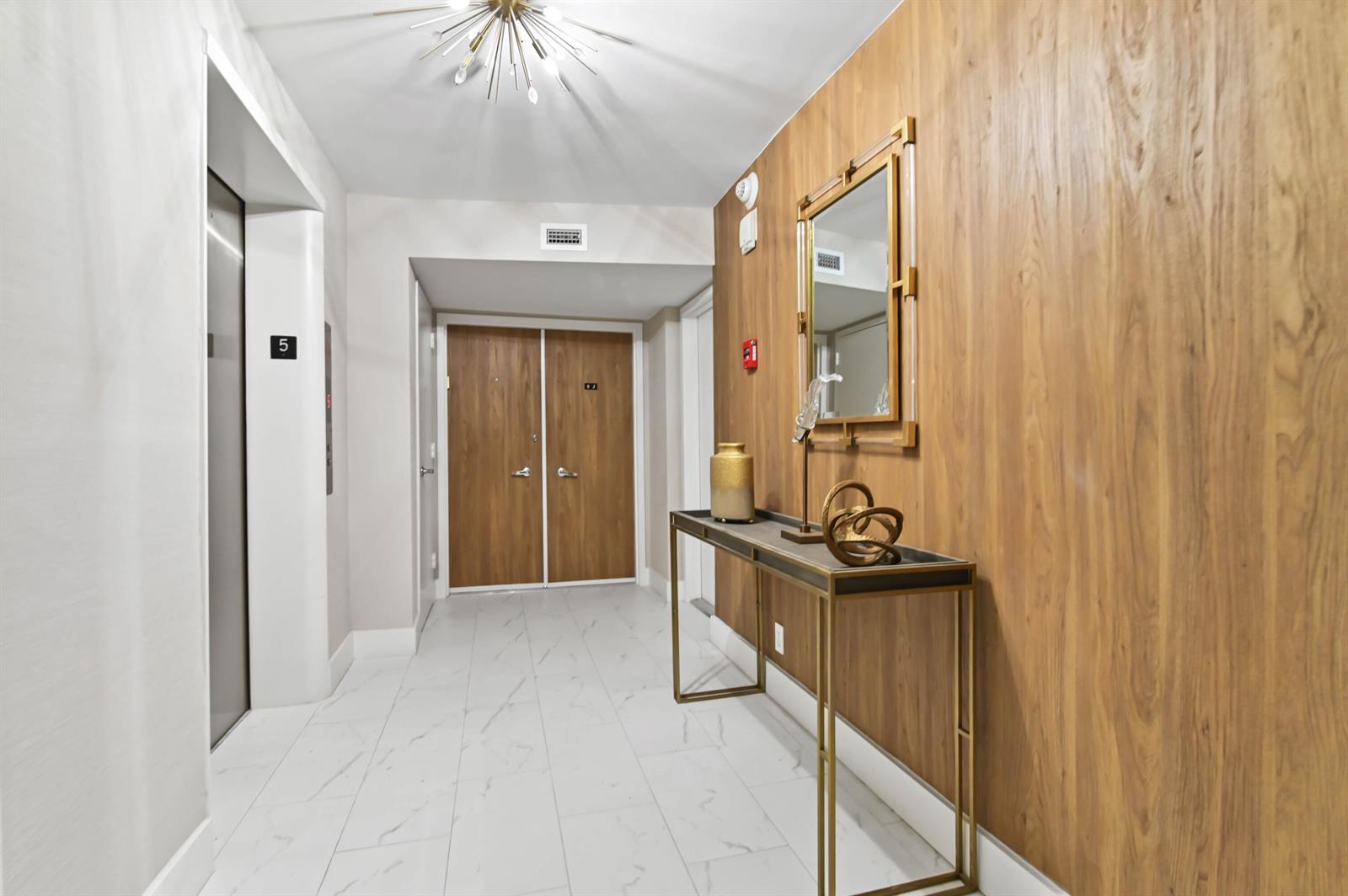 A hallway features white marble-look tile flooring, a wood-paneled wall, and a metal console table — 2800 S Ocean Boulevard Apt j, Boca Raton FL 33432, BOCA RATON, FL