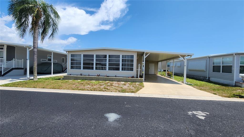 A beige mobile home features a large carport, a screened-in porch, and a palm tree — 3226 SWEET BAY TERRACE, SARASOTA, FL