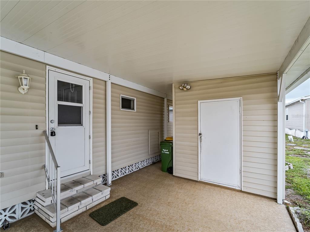 A covered carport area features a white entry door, a storage closet, and concrete flooring — 3226 SWEET BAY TERRACE, SARASOTA, FL