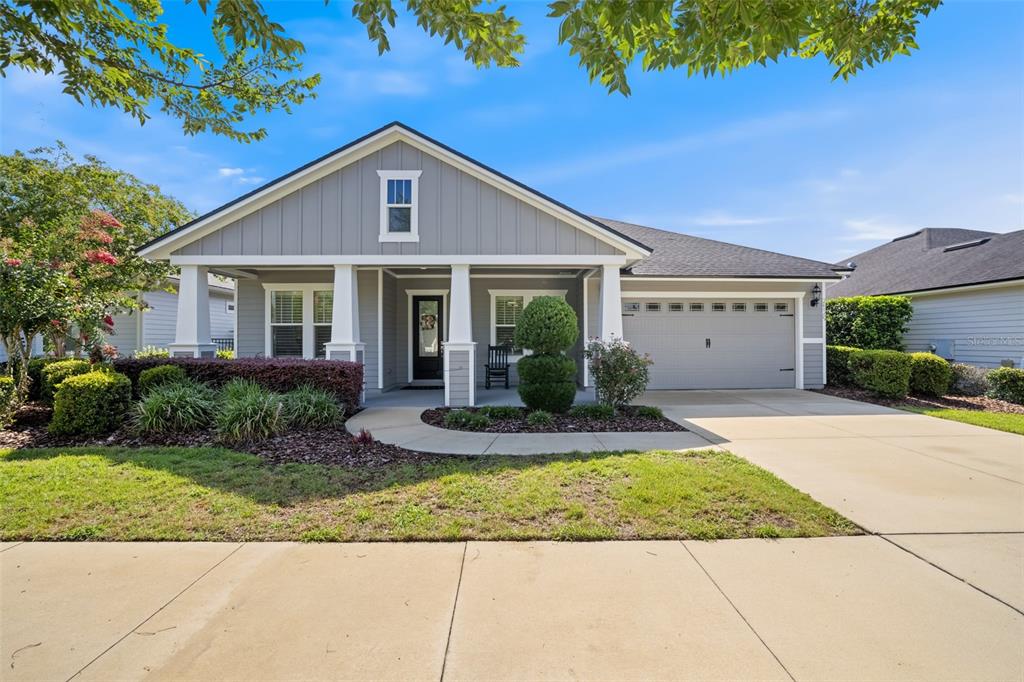 A single-story gray house with a front porch, garage, and landscaped yard under a blue sky — 2529 SW 118TH TERRACE, GAINESVILLE, FL