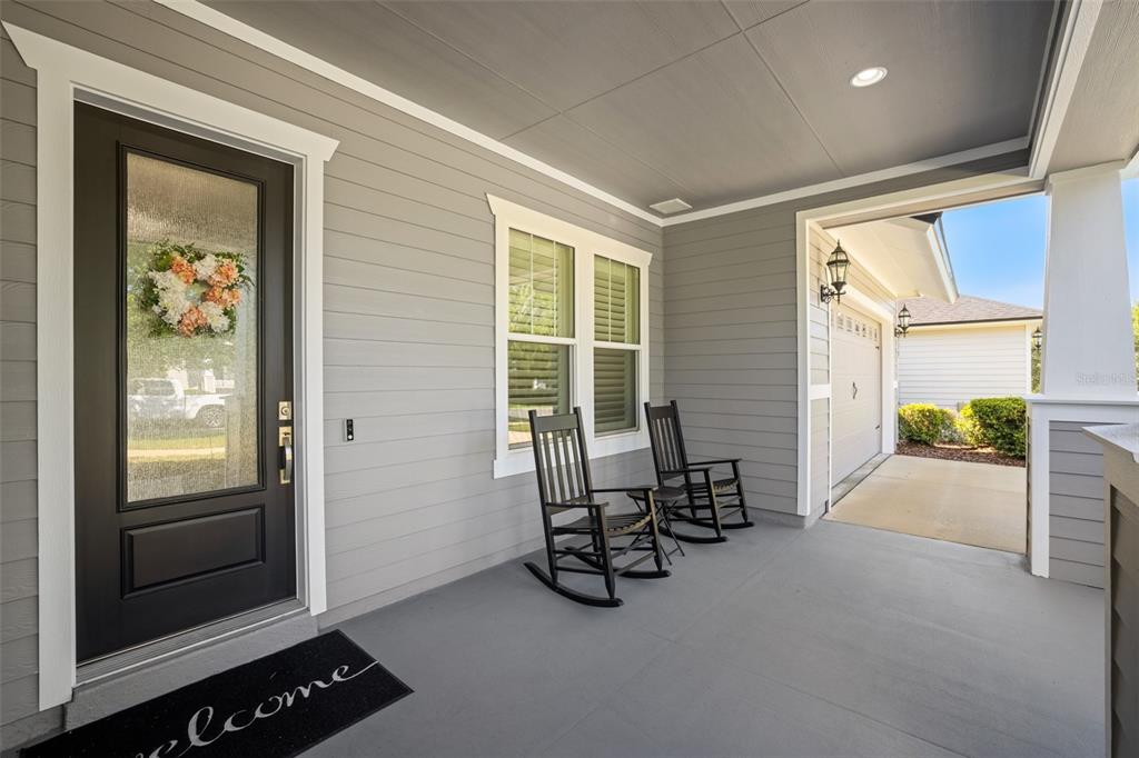 A covered front porch features gray siding, two black rocking chairs, and a front door — 2529 SW 118TH TERRACE, GAINESVILLE, FL