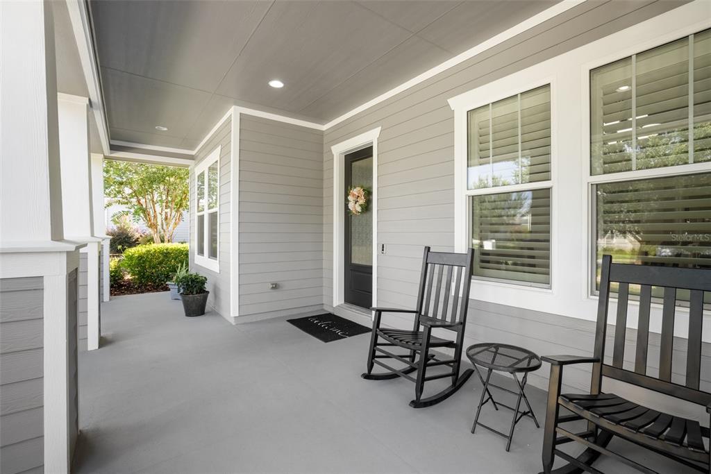 A covered front porch features gray siding, two black rocking chairs, and a small table — 2529 SW 118TH TERRACE, GAINESVILLE, FL