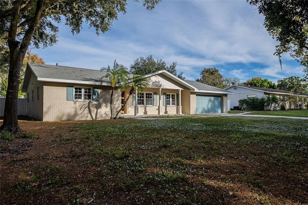 A single-story brick house with a front porch, attached garage, and a large front yard — 6212 WOODSFIELD WAY, LAKELAND, FL
