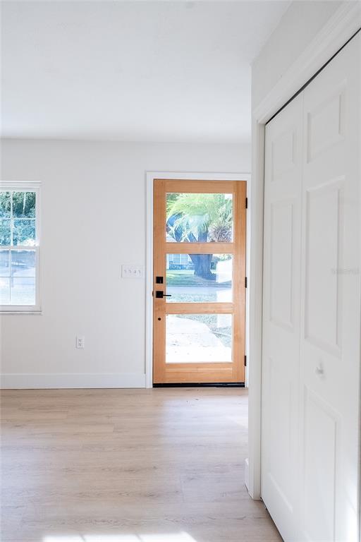 A bright room features light wood-look flooring, white walls, a closet, and a modern wood door — 6212 WOODSFIELD WAY, LAKELAND, FL