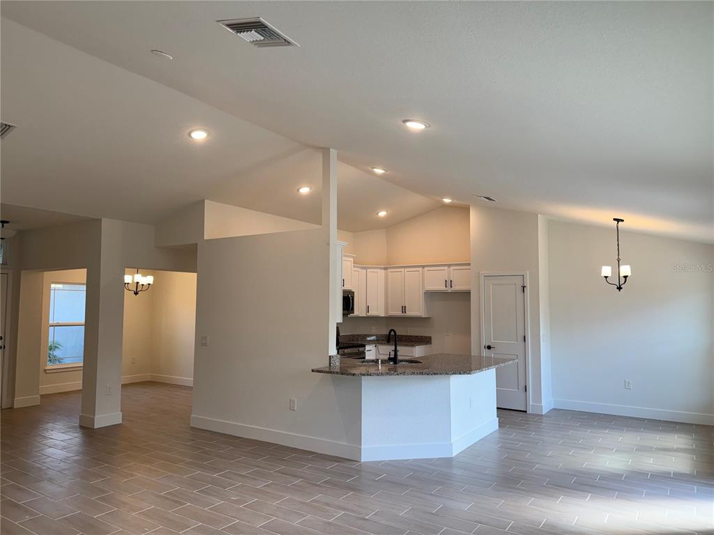 An open-concept kitchen features white cabinets, granite countertops, and light-colored tile flooring — 7933 TROPICAIRE BLVD., NORTH PORT, FL