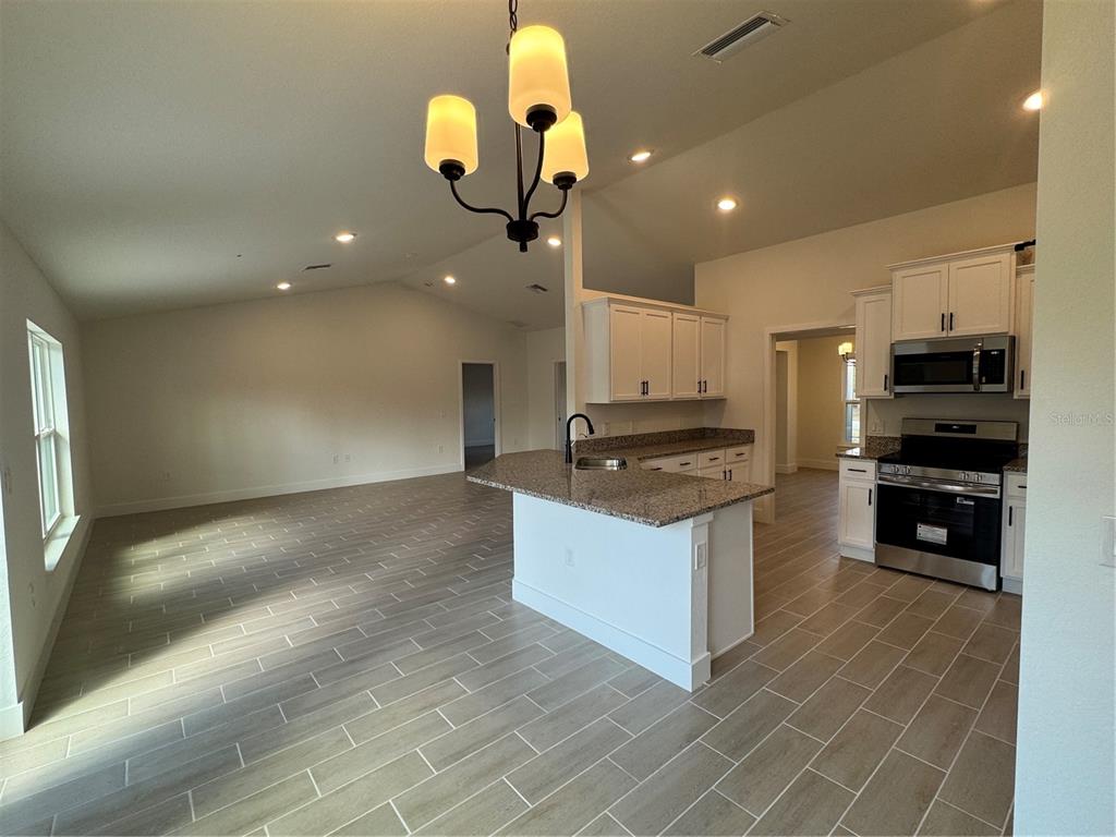 An open-concept kitchen and living area featuring white cabinets, granite countertops, and tile flooring — 7933 TROPICAIRE BLVD., NORTH PORT, FL