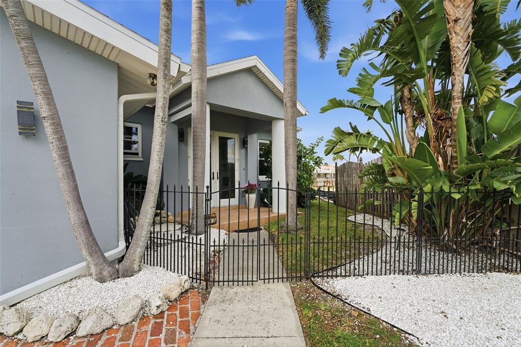A gated walkway leads to the front entrance of a house with palm trees — 16115 4TH STREET E, REDINGTON BEACH, FL