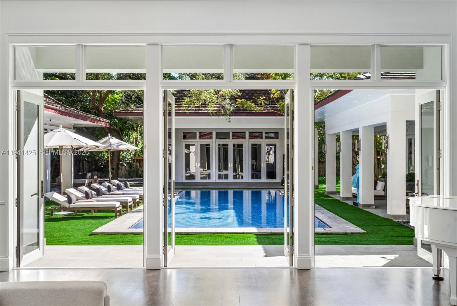 A view through open glass doors reveals a swimming pool surrounded by lounge chairs — 4100 Kiaora St, Miami FL 33133, MIAMI, FL