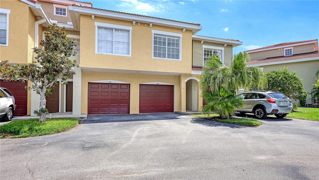 A two-story townhouse exterior with two red garage doors and a silver SUV parked outside — 5551 BENTGRASS DRIVE UNIT 11-117, SARASOTA, FL