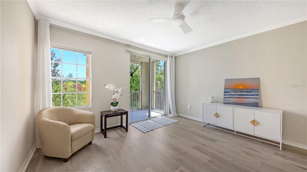 A living room features light wood flooring, a beige armchair, a white sideboard, and a balcony — 5551 BENTGRASS DRIVE UNIT 11-117, SARASOTA, FL