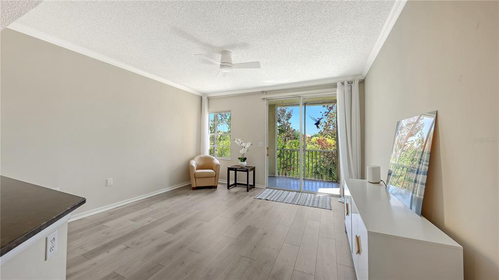 A living room with light wood-look flooring, a ceiling fan, and a sliding glass door — 5551 BENTGRASS DRIVE UNIT 11-117, SARASOTA, FL