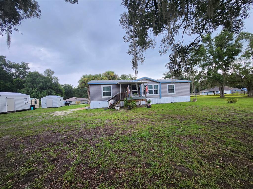 A single-story manufactured home with gray siding sits on a grassy lot with two sheds — 152 KELLY LANE, HAWTHORNE, FL