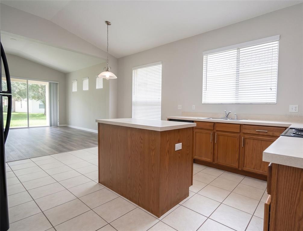 A kitchen with wood cabinets, a central island, and tile flooring overlooks a living area — 13424 HOPKINTON CT, WINDERMERE, FL