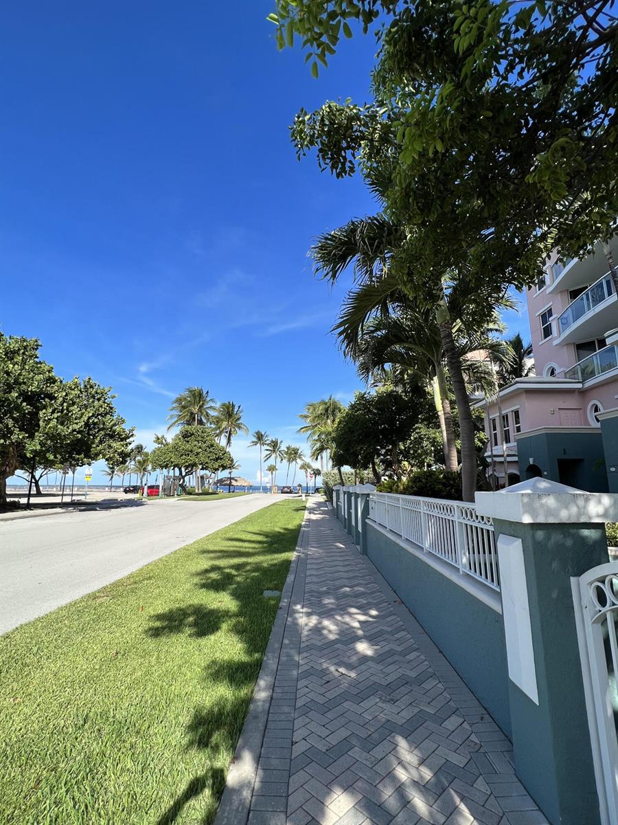 A paved sidewalk runs alongside a green lawn and a white fence near a building — 2051 SE 3rd Street, Deerfield Beach FL 33441, DEERFIELD BEACH, FL