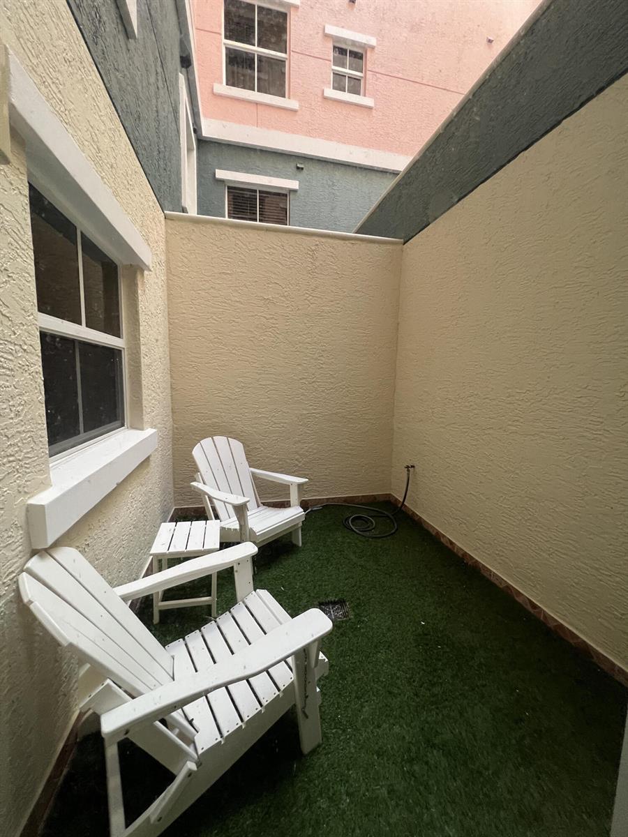 A small outdoor patio features artificial turf, two white Adirondack chairs, and a side table — 2051 SE 3rd Street, Deerfield Beach FL 33441, DEERFIELD BEACH, FL