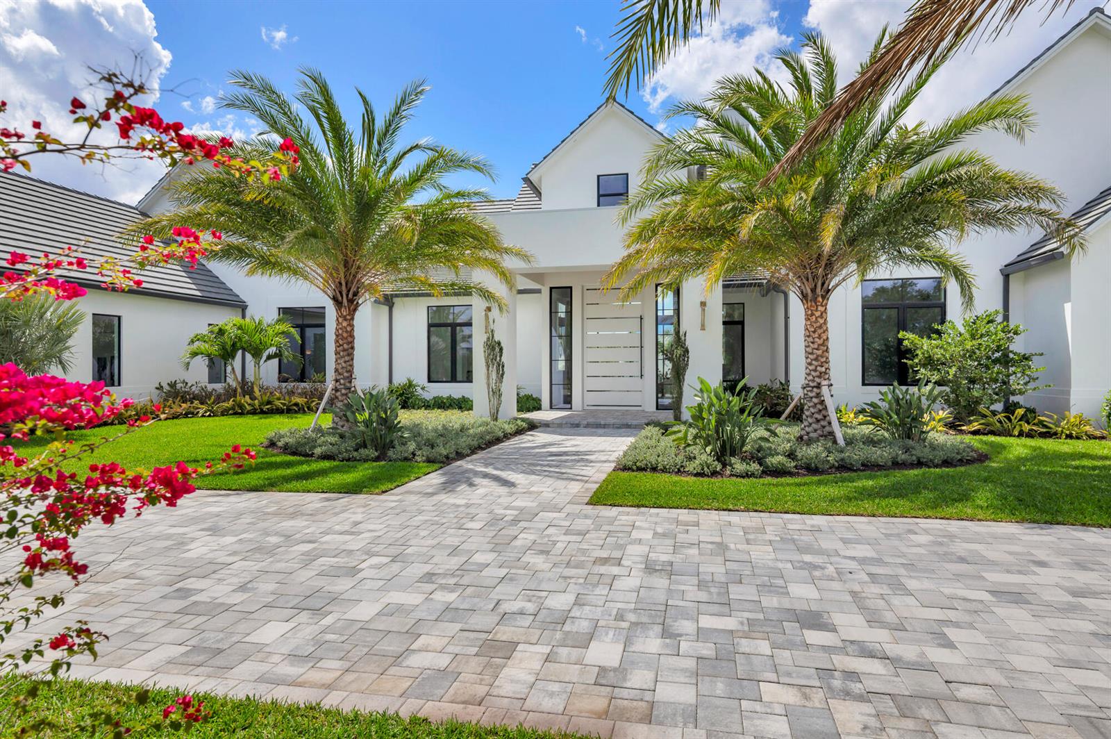 A white modern house features a paved driveway, two palm trees, and bright pink flowers — 2015 Lockheed Terrace, Wellington FL 33414, WELLINGTON, FL