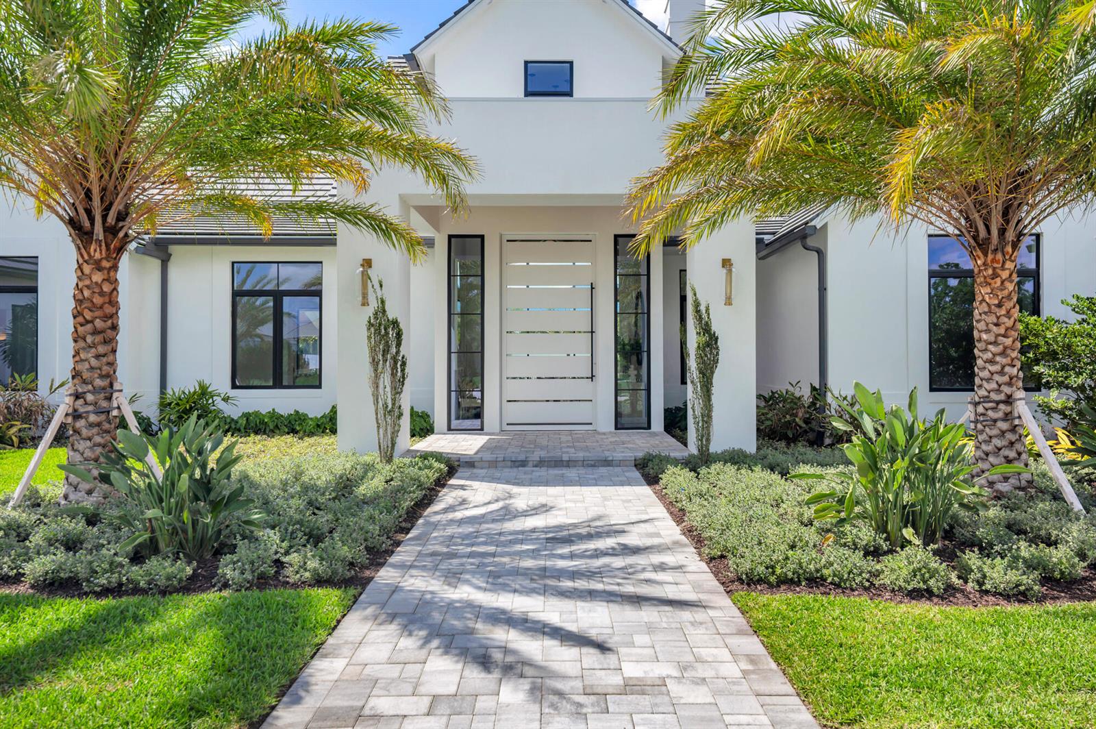 A paved walkway leads to the white front entrance of a modern house with palm trees — 2015 Lockheed Terrace, Wellington FL 33414, WELLINGTON, FL