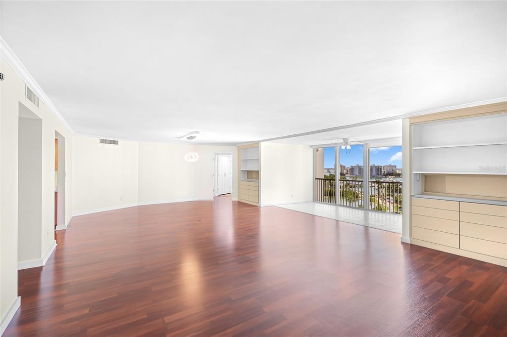 A spacious living room features hardwood floors, built-in shelving, and a balcony with water views — 435 S GULFSTREAM AVENUE UNIT 1004, SARASOTA, FL