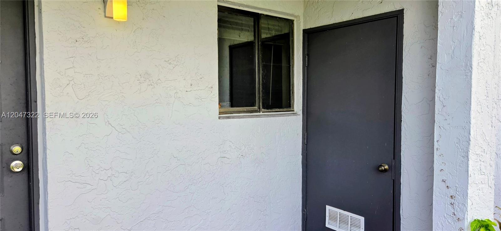 A white stucco exterior wall features a dark door, a window, and a light fixture — 153 Lakeview Dr # 104, Weston FL 33326, WESTON, FL