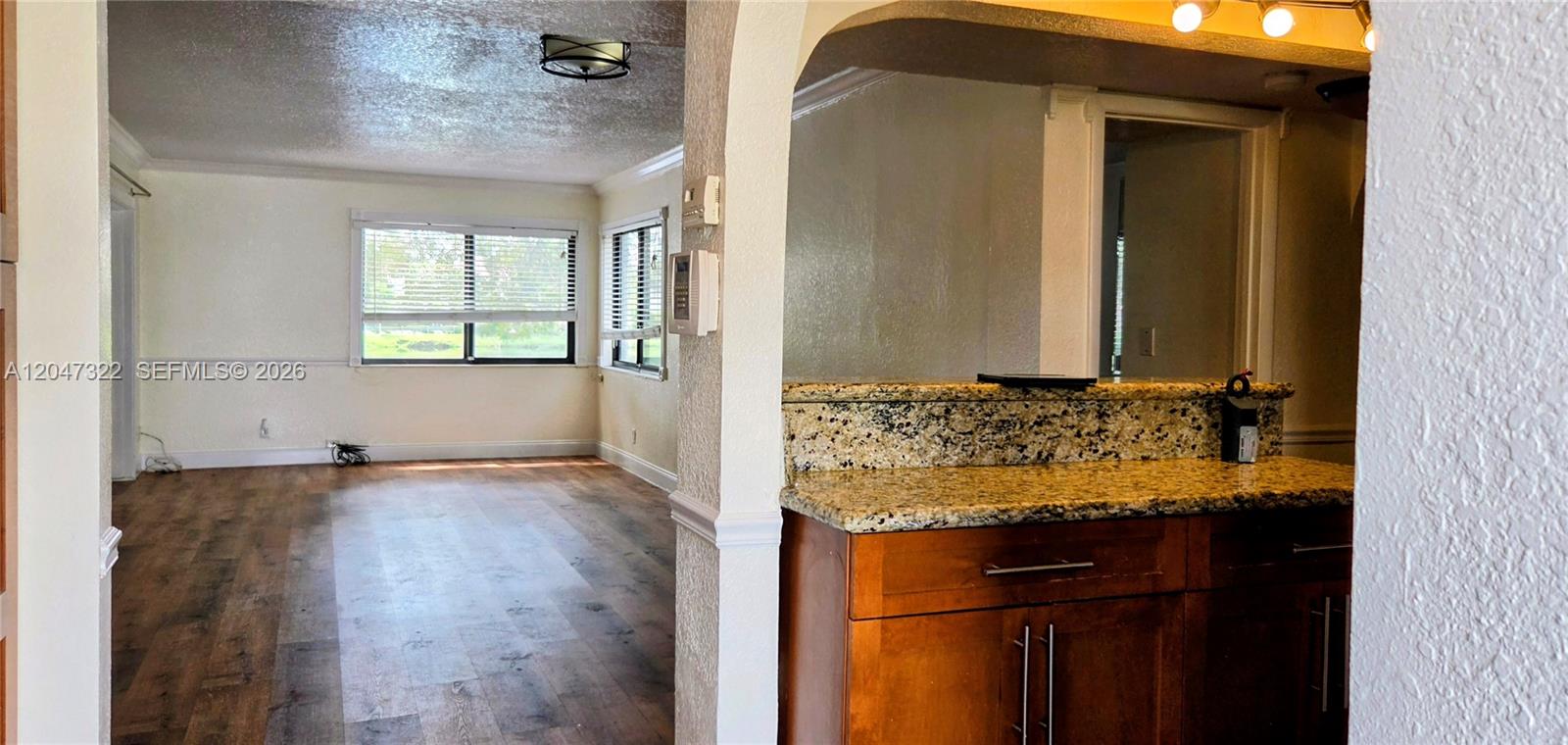 A kitchen with granite countertops overlooks a living area with wood-look flooring and windows — 153 Lakeview Dr # 104, Weston FL 33326, WESTON, FL