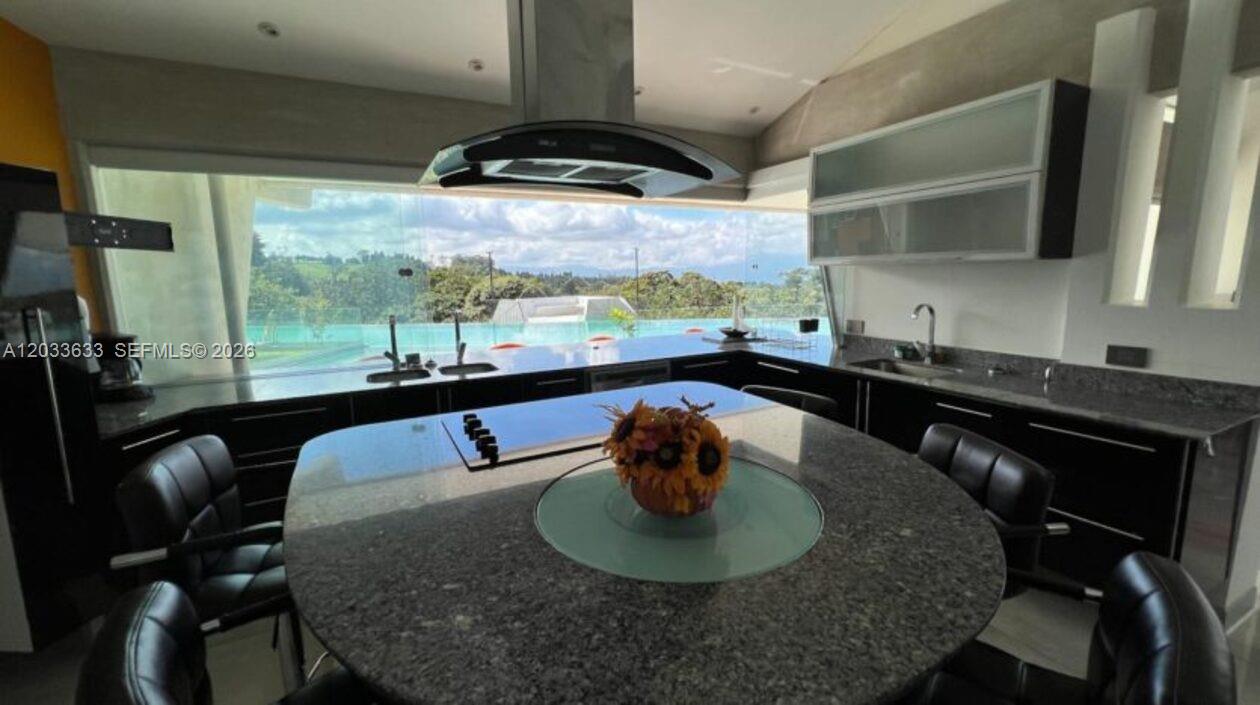 A modern kitchen features a granite island, dark cabinetry, and a large window overlooking trees — Calle Las marias Calle Las marias, FL, FL