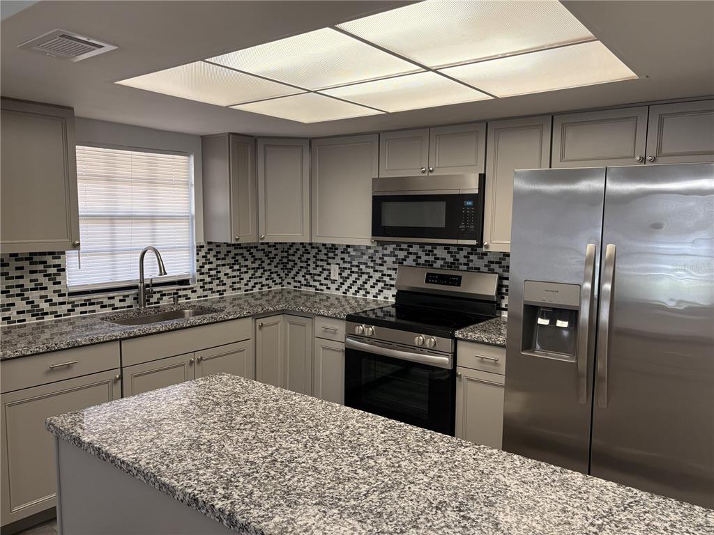 A kitchen features grey cabinets, granite countertops, a mosaic backsplash, and stainless steel appliances — 4015 ASHFORD GREEN PLACE UNIT D202, TAMPA, FL