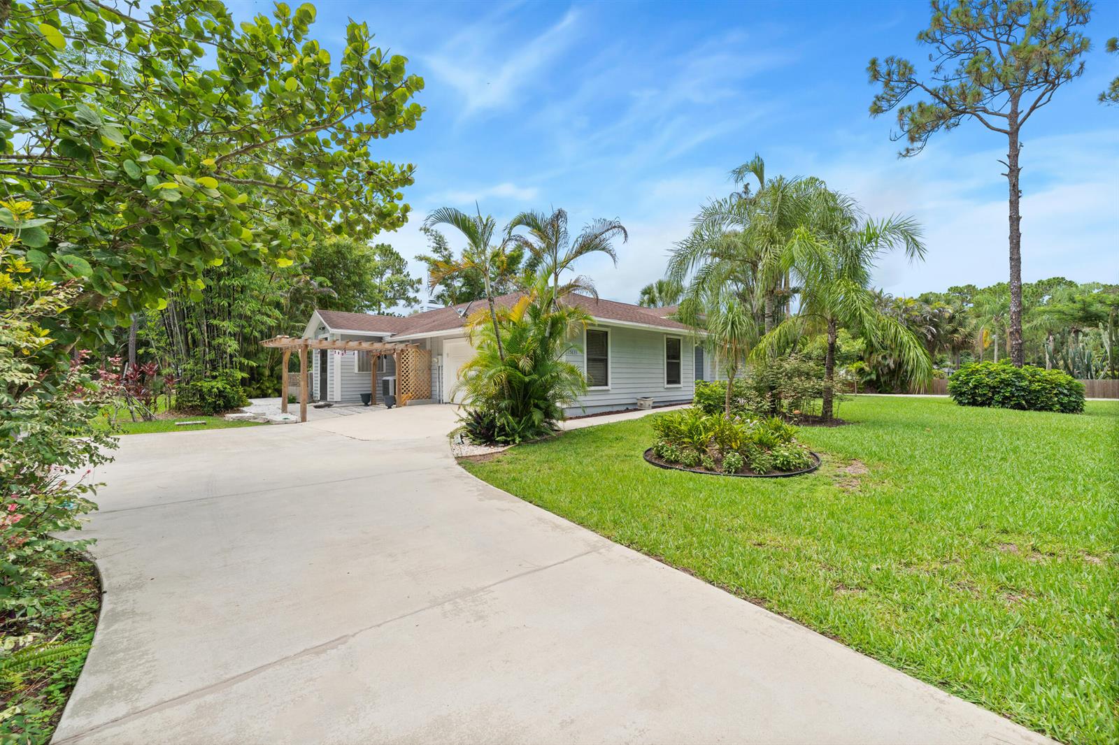 A single-story house with light gray siding, a concrete driveway, and lush tropical landscaping — 15833 118th Trail N, Jupiter FL 33478, JUPITER, FL