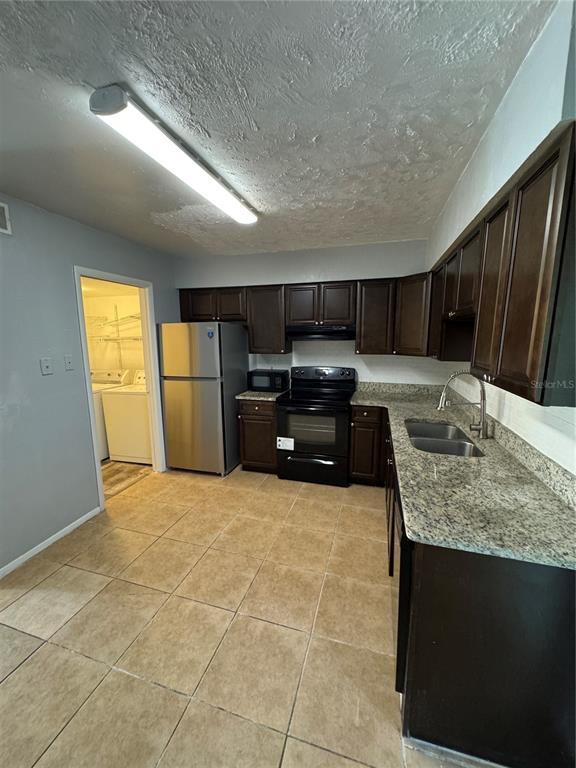 A kitchen features dark wood cabinets, granite countertops, stainless steel appliances, and beige tile flooring — 3976 CRAYRICH CIRCLE UNIT C1, ORLANDO, FL