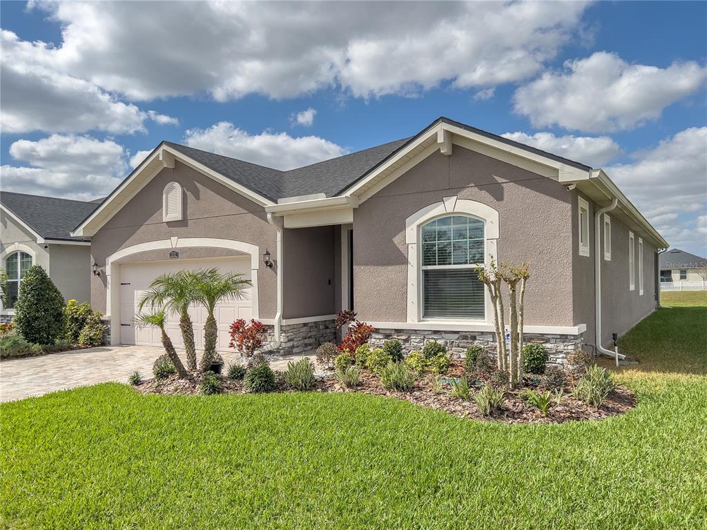 A single-story house with a beige stucco exterior, stone accents, and a two-car garage — 13102 SATIN LILY DRIVE, RIVERVIEW, FL