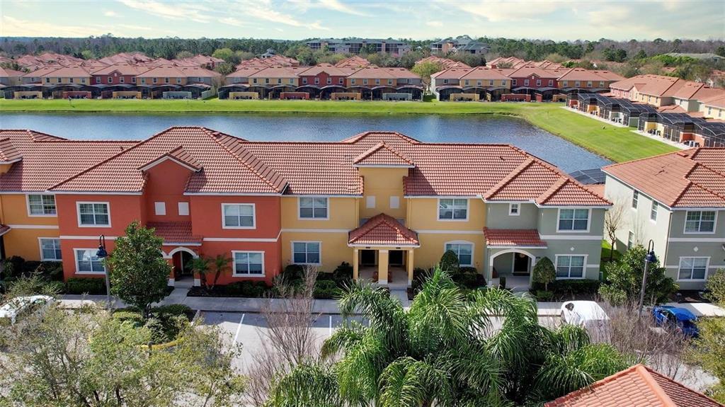 An aerial view shows a multi-story apartment complex with red-tiled roofs near a lake — 8859 CANDY PALM ROAD, KISSIMMEE, FL