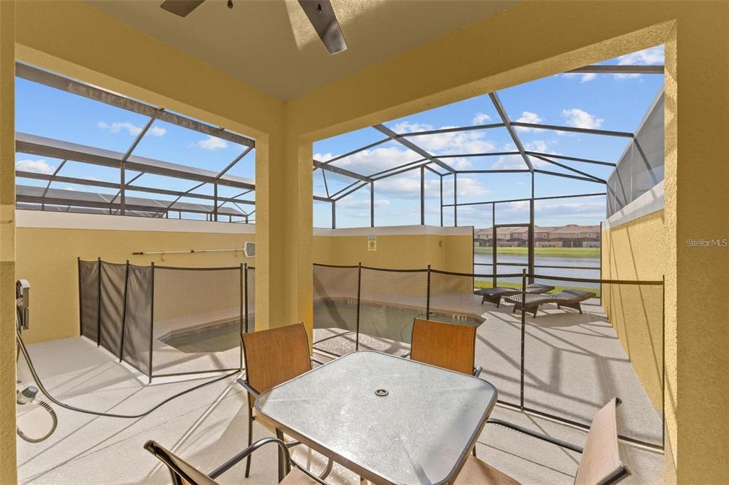 A covered patio features a dining set, a safety fence, and a screened-in swimming pool — 8859 CANDY PALM ROAD, KISSIMMEE, FL