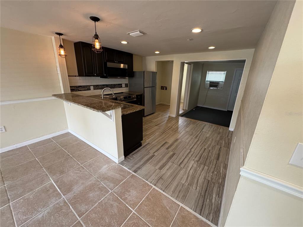 A kitchen features dark cabinets, granite countertops, a breakfast bar, and wood-look tile flooring — 2111 FORKED CREEK DRIVE, ENGLEWOOD, FL