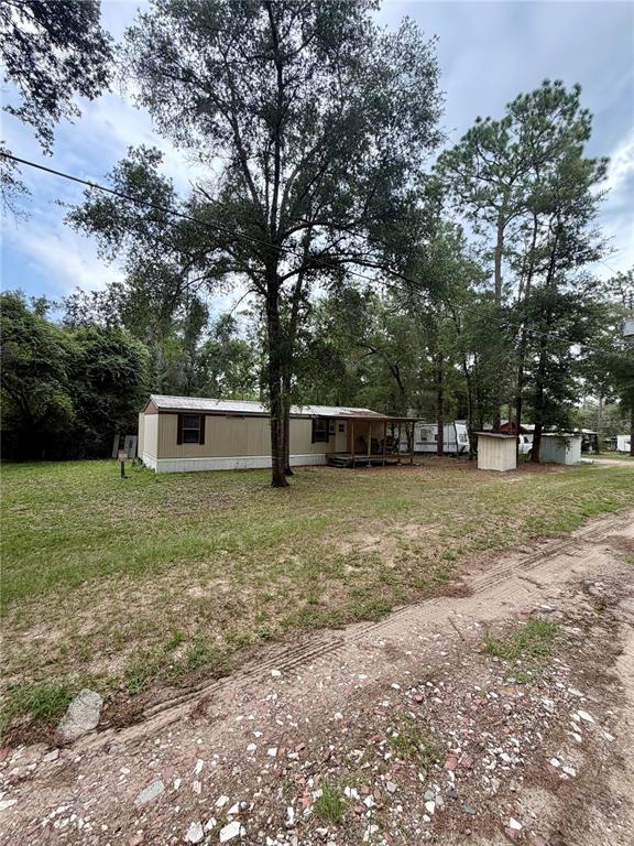 A tan mobile home with a small front porch sits on a grassy, wooded lot — 20445 NE 144TH LANE, FORT MC COY, FL
