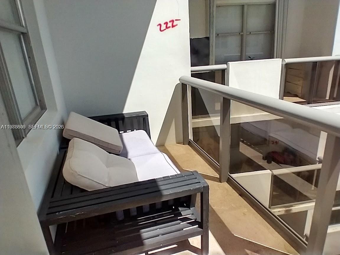 A balcony features a dark wooden bench with light-colored cushions and a metal railing — 6039 Collins Ave # 1710, Miami Beach FL 33140, MIAMI BEACH, FL