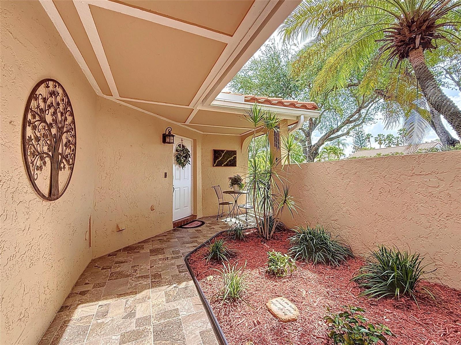A covered patio features tiled flooring, a decorative tree wall hanging, and a small garden — 1420 Seagrape Circle, Weston FL 33326, WESTON, FL