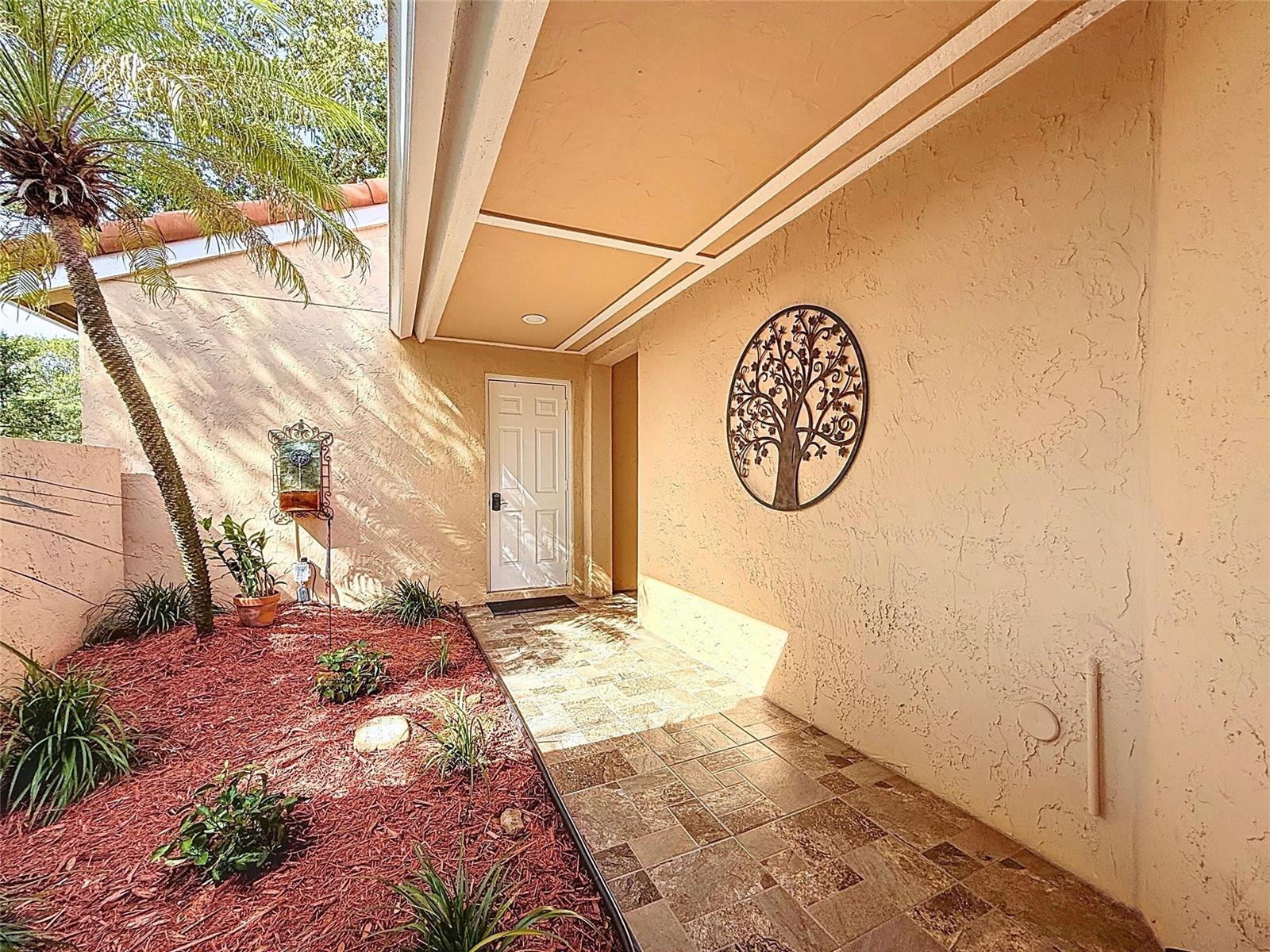 A tiled walkway leads to a white front door beside a tree-shaped wall decoration — 1420 Seagrape Circle, Weston FL 33326, WESTON, FL