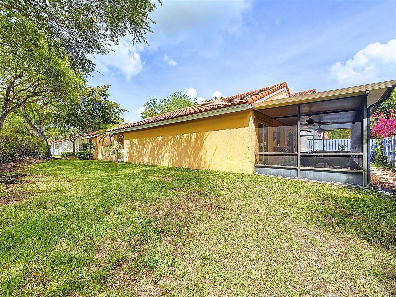 The exterior of a yellow house features a screened-in patio and a grassy backyard — 1420 Seagrape Circle, Weston FL 33326, WESTON, FL